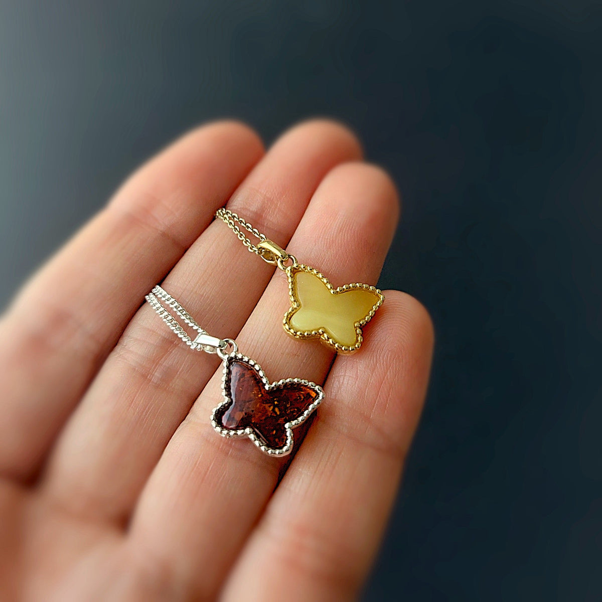 Butterfly-shaped pendants on a chain held in a hand against a dark background