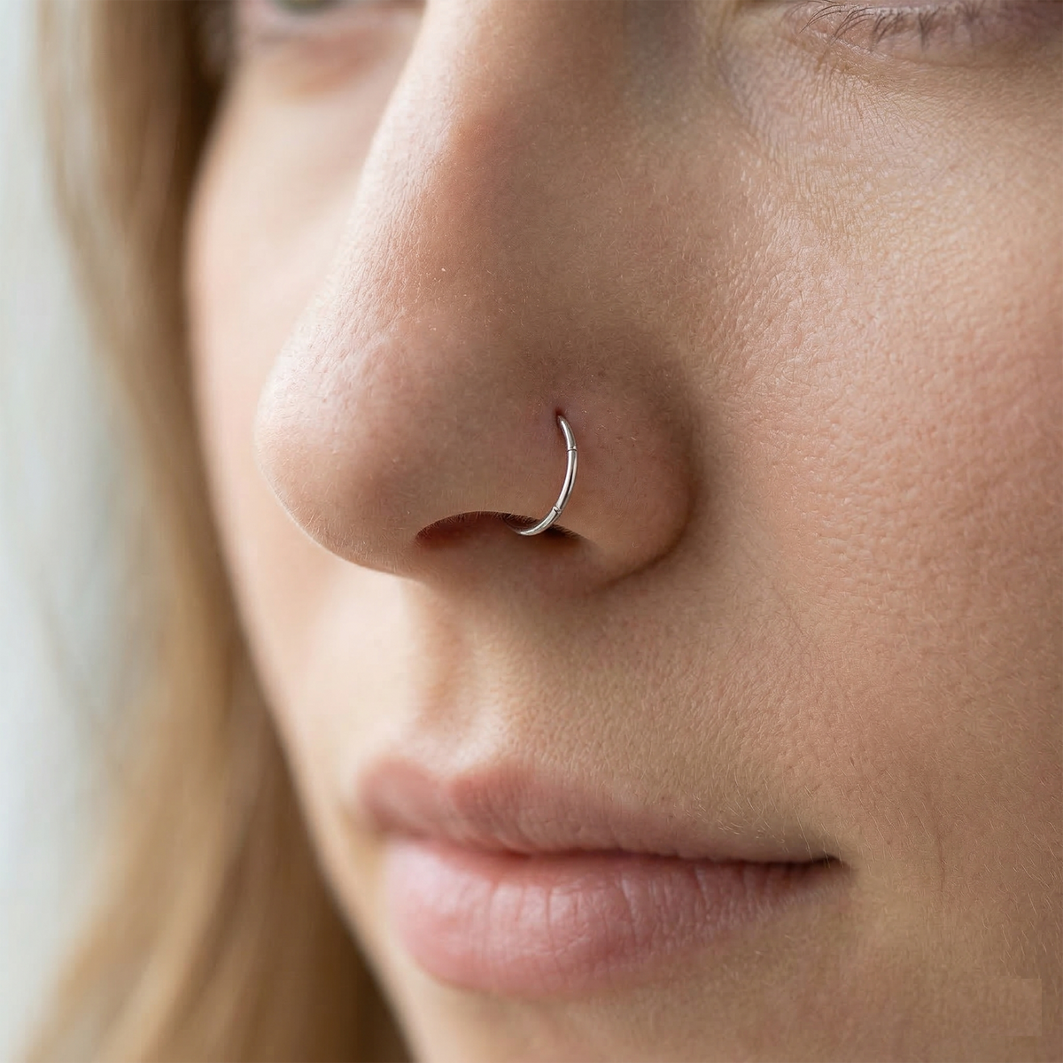 Silver hinged hoop shown on nostril piercing