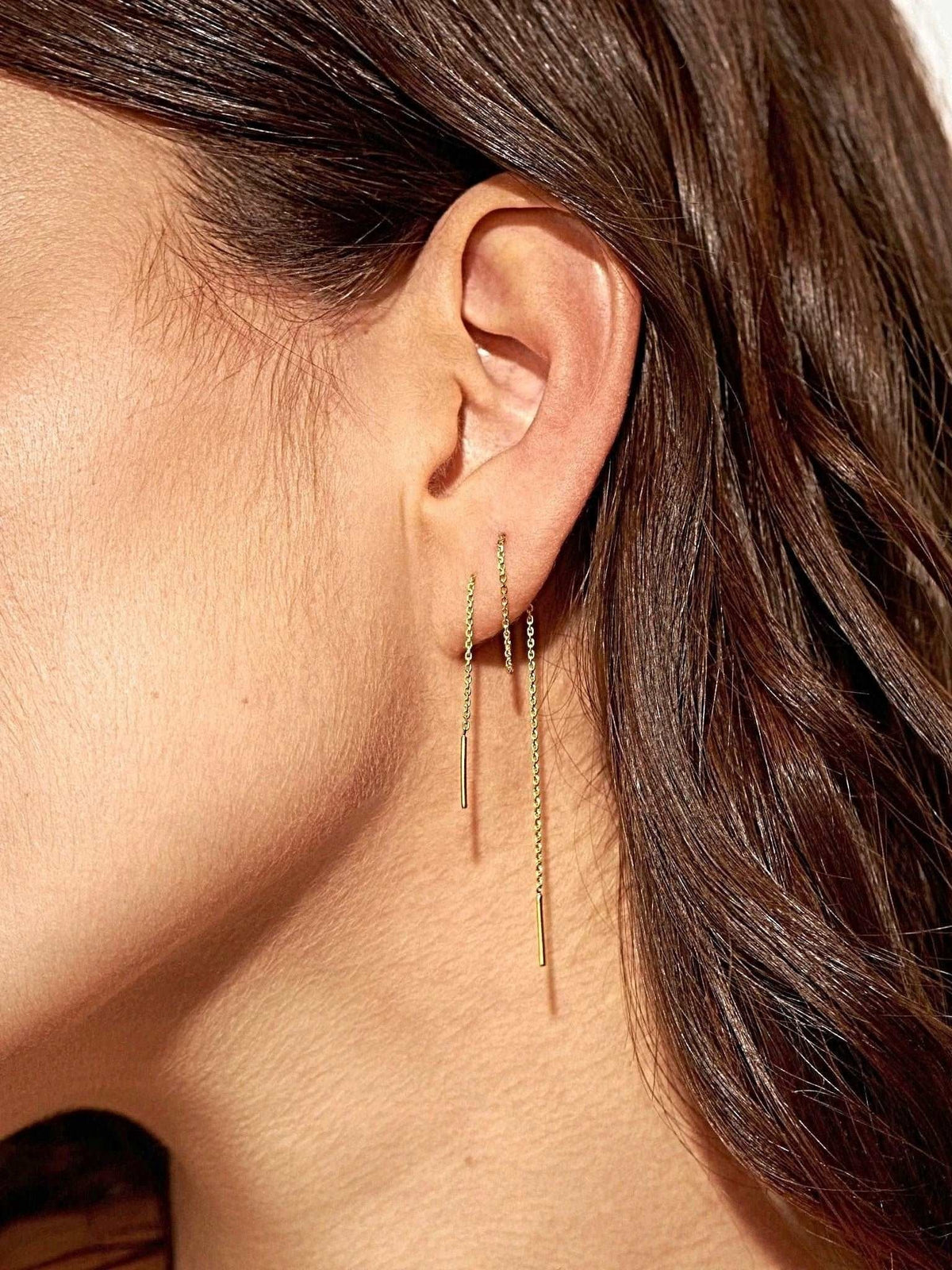 Woman wearing 24K gold plated ear thread earrings, 14 cm length, thin chain with small bar ends, side view of the ear