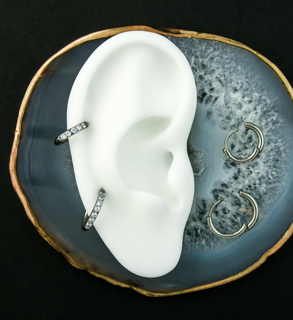 Titanium Clear CZ Hinged Hoop Huggie Earrings, in two helix piercings on a white display ear with spares