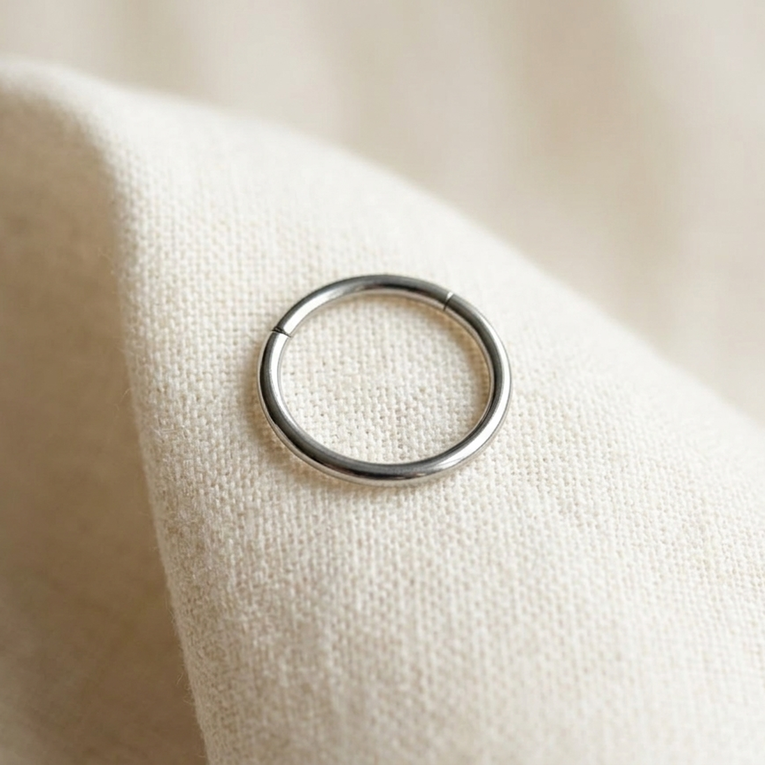 Silver hinged hoop ring on cream linen fabric