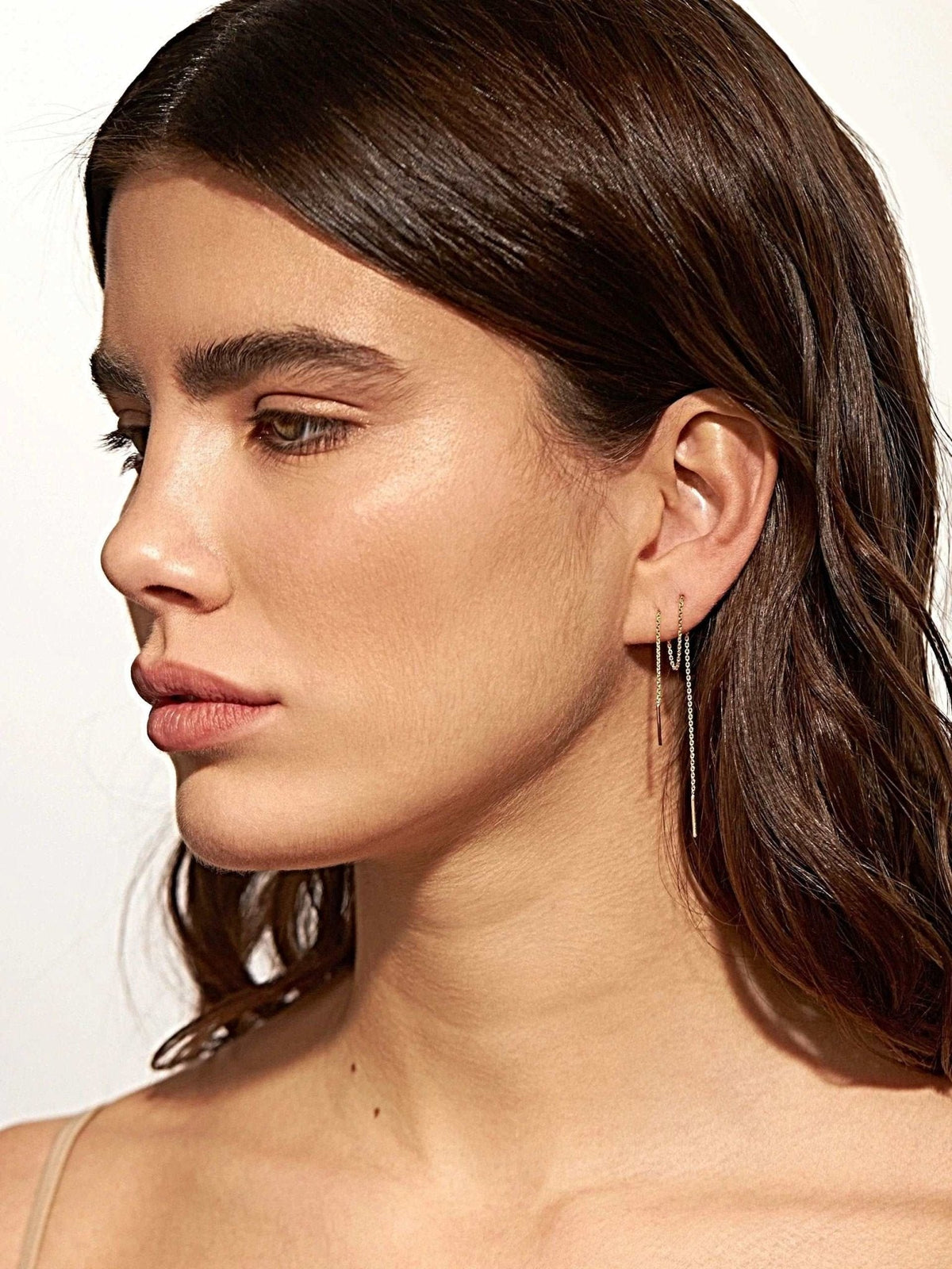 Woman wearing 18K rose gold plated ear thread earrings, 14 cm length, thin chain with small bar ends, profile view